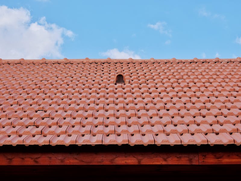 Tiled roof with a vent and flashing against a blue sky